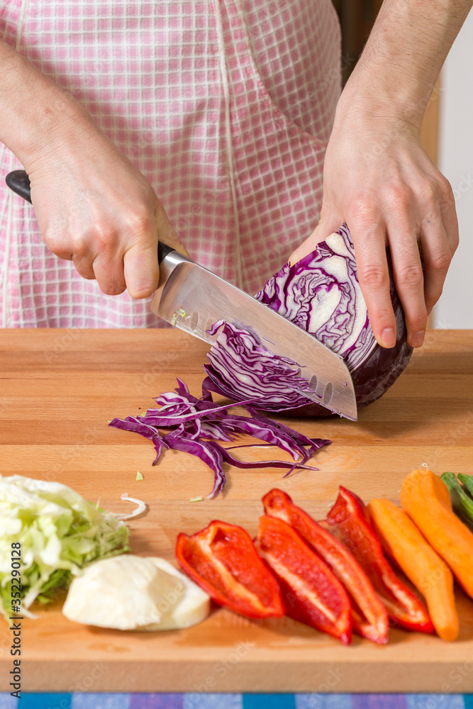 Close up of hands chopping red cabbage on a wooden board. Healthy food preparation concept