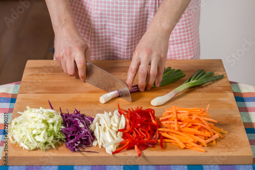 Close up of hands chopping scallions on a wooden board. Healthy food preparation concept