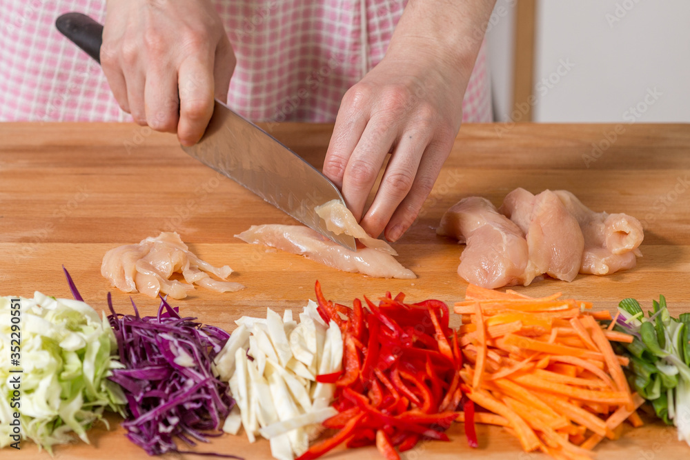 Close up of hands slicing chicken breast on a wooden board. Healthy food preparation concept