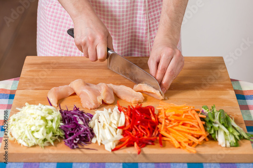 Close up of hands slicing chicken breast on a wooden board. Healthy food preparation concept