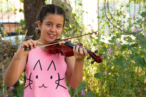 Brunette teenager with braids in her hair playing the violin. Concept children playing instruments in nature.