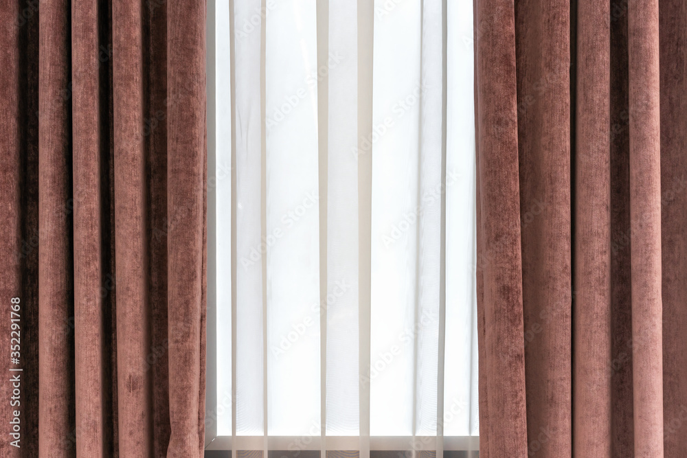 Fototapeta premium Brown velor curtains and white tulle on the window in the living room.