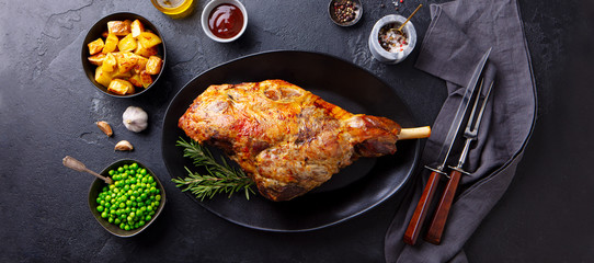 Roasted lamb leg with potato and green peas. Black background. Top view.