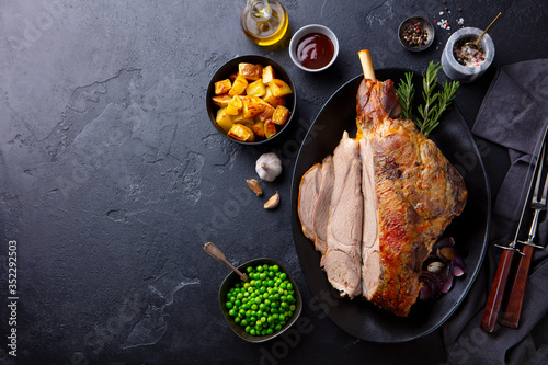Roasted lamb leg with potato and green peas. Black background. Copy space. Top view.