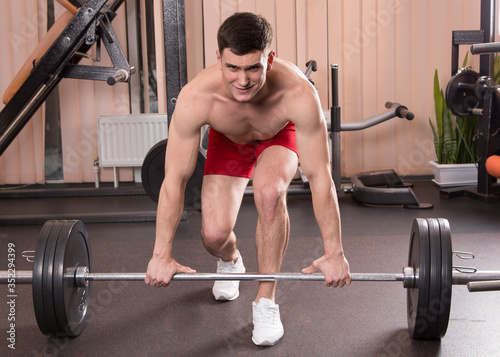 Young man flexing muscles with barbell in gym.