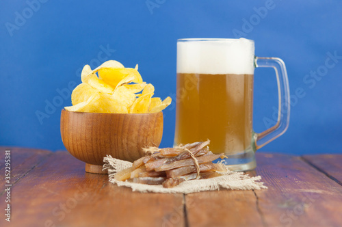 Beer glass with beer and smoked fish close-up. Beer mug with beer and potato chips, crackers on a wood background and copy space.