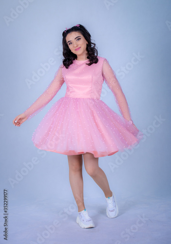 Portrait Of Beautiful Young girle Standing Against blue Background,girl in a pink dress,Happy cheery smiling young cute girl posing isolated,White running shoes