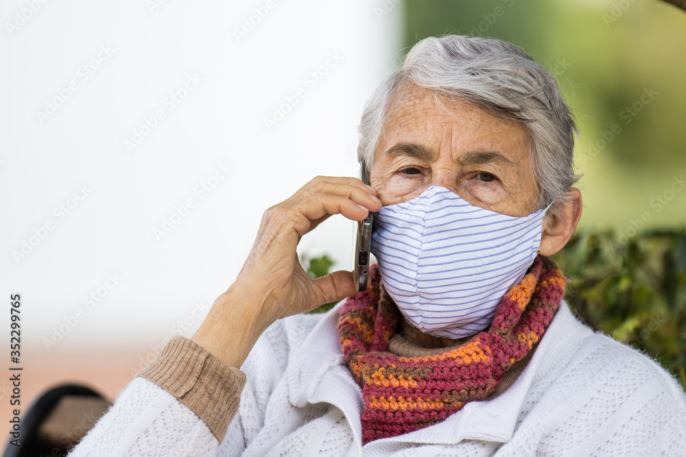 Senior woman outdoors using her cell phone wearing a home made face mask during the coronavirus quarantine de-escalation Senior woman outdoors using her cell phone wearing a home made face mask during the coronavirus quarantine de-escalation