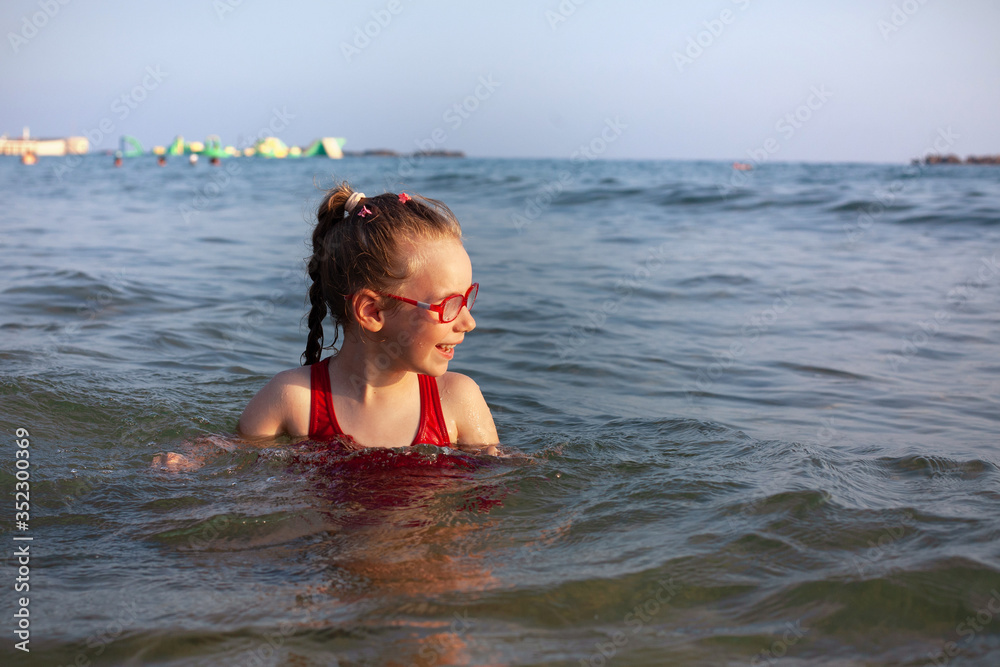 young girl in glasses bathes in the blue sea