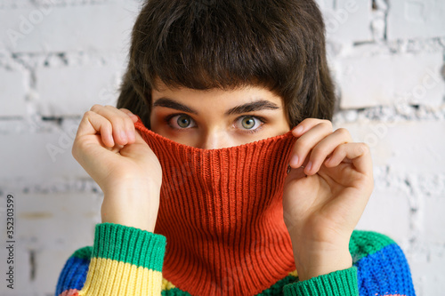 Portrait of a young woman in a multicolored sweater, covering her face with a sweater . The concept of shyness photo