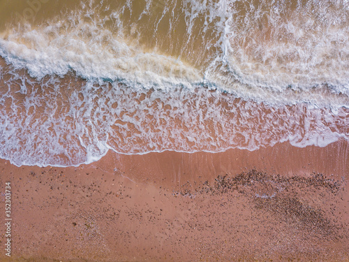 Top down view of waves breaking in the sand, flying over tropical sandy beach and waves