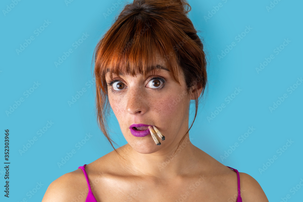 Young woman with red hair smoking two cigarettes at the same time on blue background Young woman with red hair smoking two cigarettes at the same time on blue background