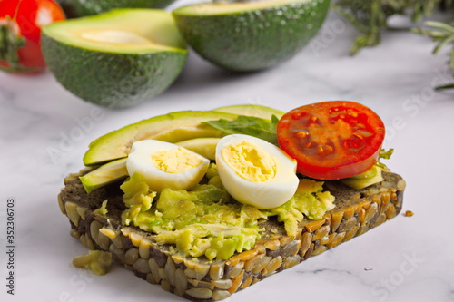 Healthy whole-grain bread with avocado, tomatoes and quail eggs on the bright kitchen table.