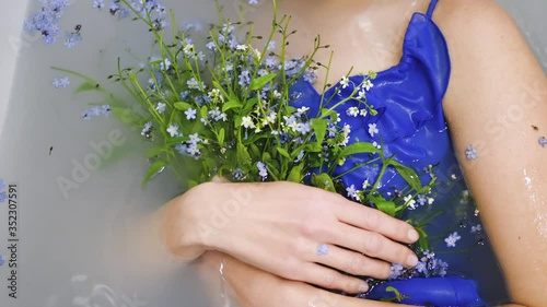 fashion woman in a blue dress and a bouquet of blue flowers lies in the bathroom with milk