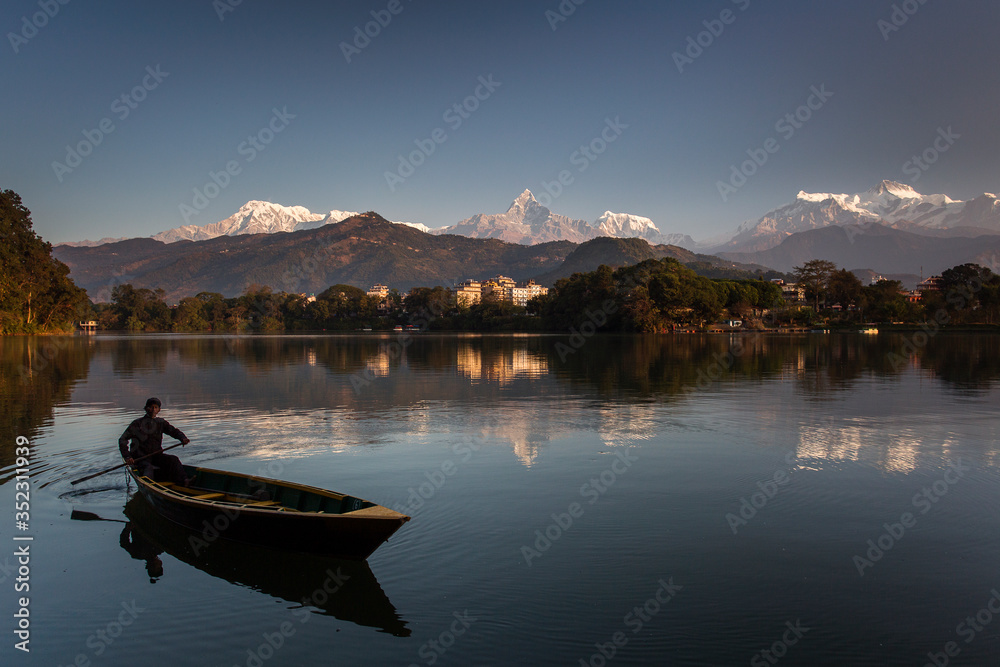 Beautiful landscape with Phewa Lake and boat on lake, mountains in background also as reflectaion on lake.  Machapuchare-FIshtail, Annapurna and many others. Pokhara, Nepal