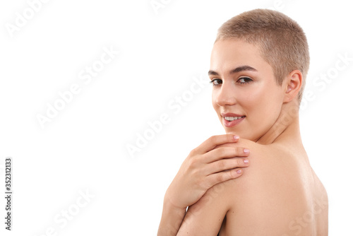 Portrait of young and cute half naked blond woman with short hair looking at camera and keeping hand on her shoulder while standing against white background