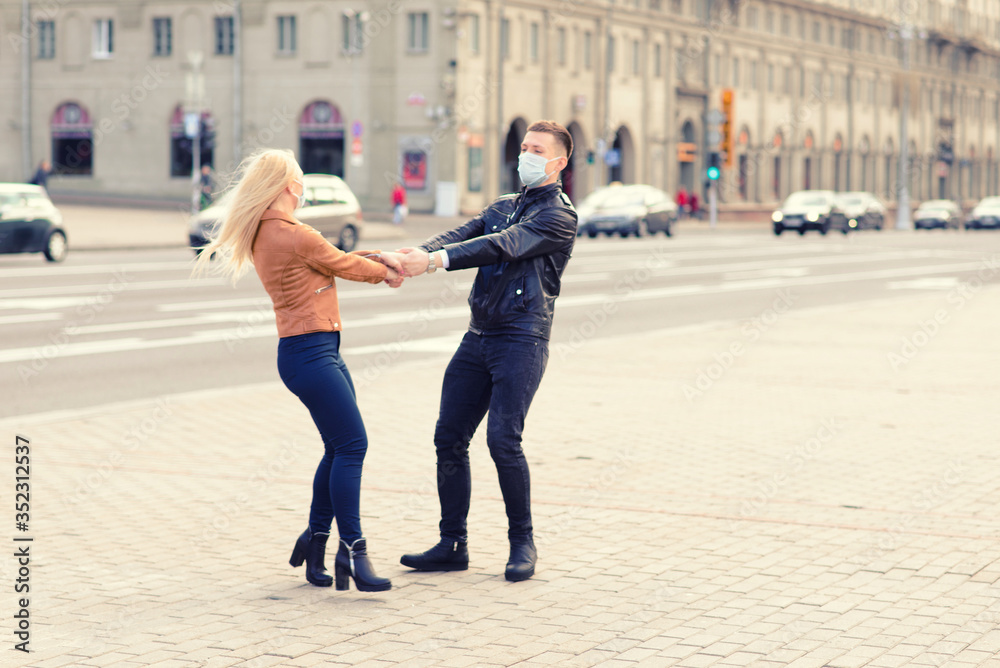 Couple in protective masks have a walk outdoors in the city near business building at quarantine time. Conception of coronavirus. Couple in protective masks have a walk outdoors in the city near business building at quarantine time. Conception of coronavirus.