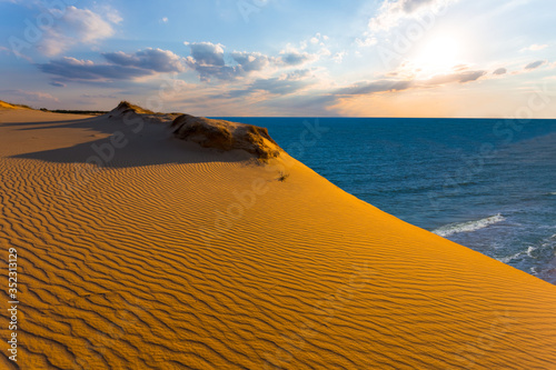 Fotografie high sandy dune above a sea bay at the sunset, evening sea landscape