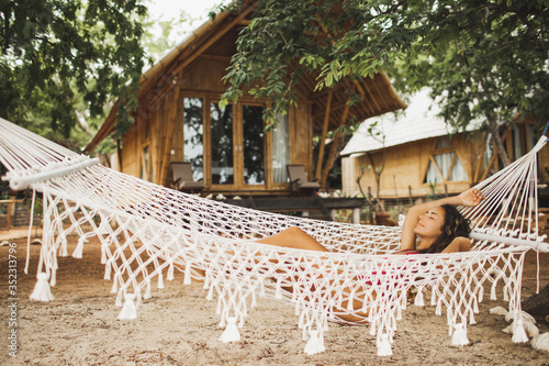 Woman relaxing in the white handmade macrame hammock on tropical beach. Travel, leisure and vacations concept. photo