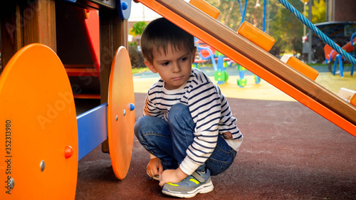 Sad little boy hiding under slide on children playground at kindergarten