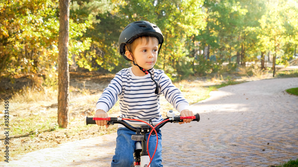 Naklejka premium Little toddler boy riding bicycle on path at park