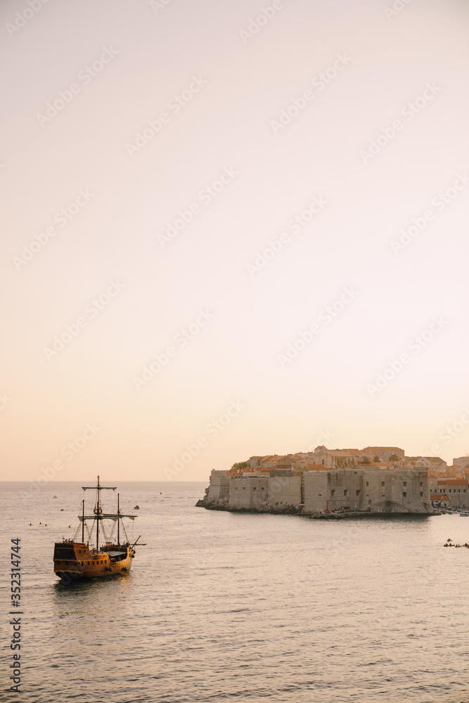 The old city of Dubrovnik against the sunset sky. The wooden sailing ship Galleon approaches the main pier of Dubrovnik.