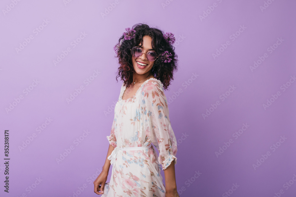 Ecstatic black girl in trendy dress posing with happy smile. Studio photo of glad african female model wears flowers in wavy hair. Ecstatic black girl in trendy dress posing with happy smile. Studio photo of glad african female model wears flowers in wavy hair.
