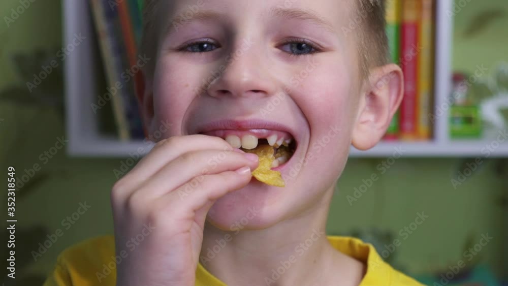 Young caucasian kid eating unhealthy potatoes crisps. Smiling boy enjoys chips. Child puts potato chips in his mouth. Snack on junk food. Portrait of a boy with a satisfied face. Tasty food. Young caucasian kid eating unhealthy potatoes crisps. Smiling boy enjoys chips. Child puts potato chips in his mouth. Snack on junk food. Portrait of a boy with a satisfied face. Tasty food.