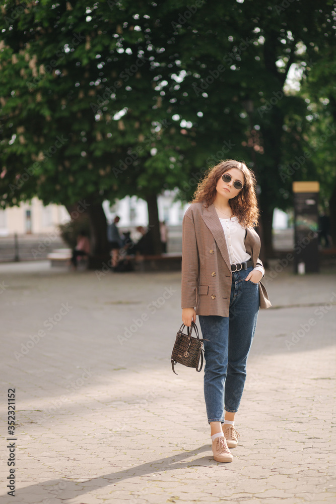 Portrait of attractive woman with curly hair in sunglasses outdoors. Happy young woman walking in the city