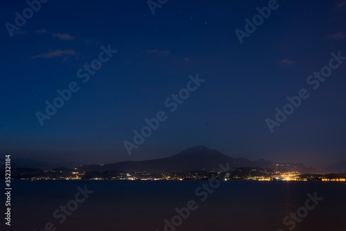 Night shot from a coast of Peschiera del Garda to the Garda lake and mountains with lights all over the other coast. Lights of Garda town in the night from other coast.