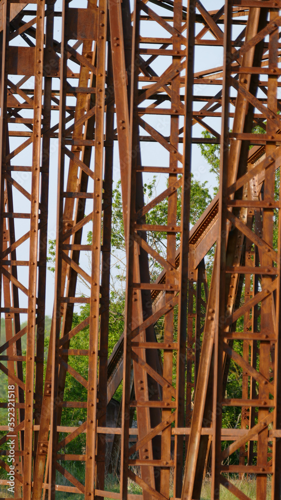 An old disused rusted brown bridge in the countryside connecting two banks across a river, formerly used for busy agricultural traffic An old disused rusted brown bridge in the countryside connecting two banks across a river, formerly used for busy agricultural traffic