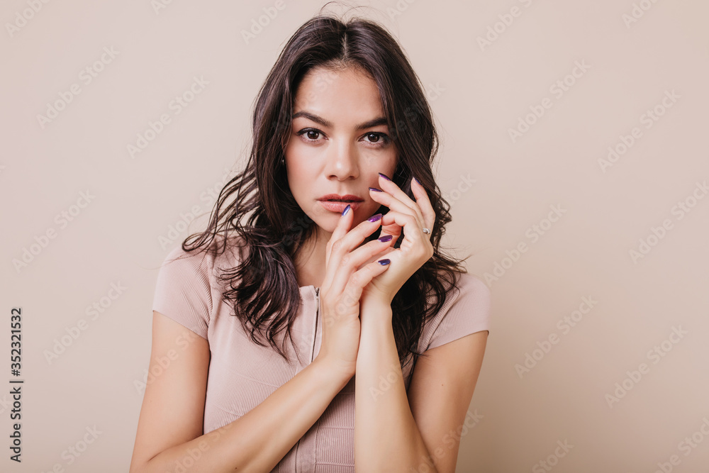 Сharming girl with long eyelashes looks into camera. Closeup portrait of brunette with beautiful purple manicure on beige background
