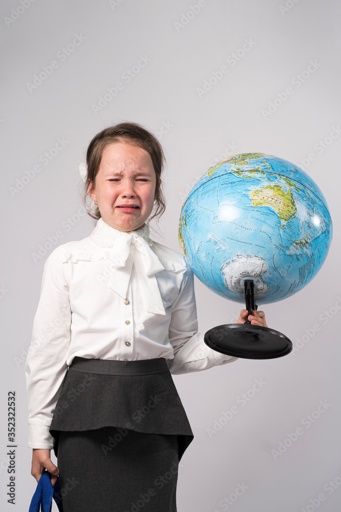 first grade school girl in a white shirt holds a globe in her hands and cries first grade school girl in a white shirt holds a globe in her hands and cries