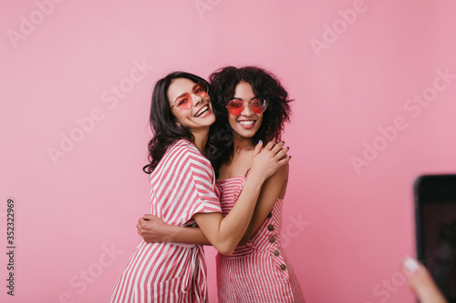 Debonair girls in pink sunglasses embracing and smiling. Gorgeous black female model enjoying photoshoot in summer day