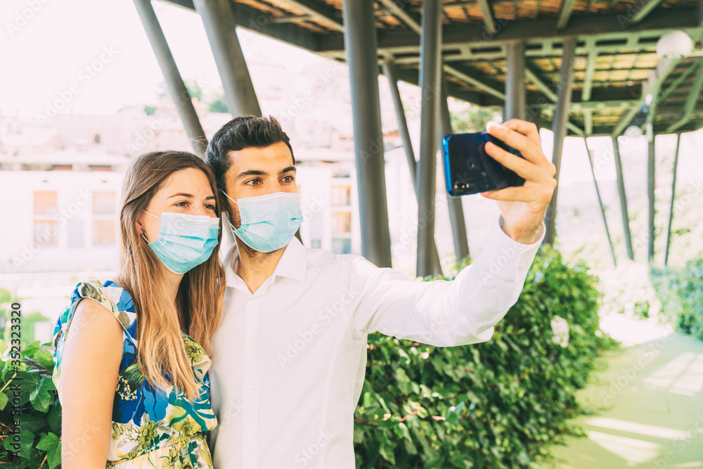young tourist couple takes a photo with a medical mask in a green urban background