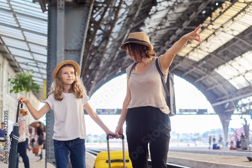 Happy mother and daughter child walking together at railway station with suitcase