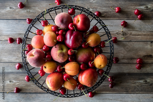 Horizontal view of a metal bowl filled with stone fruit against a wooden table. photo