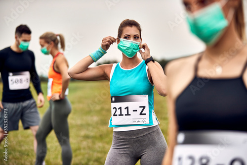 Fototapeta Naklejka Na Ścianę i Meble -  Female marathon runner putting on a face mask during corona virus epidemic.