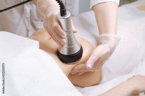 Beautician makes the procedure cavitation of a young beautiful girl. The concept of skin care face and body photo
