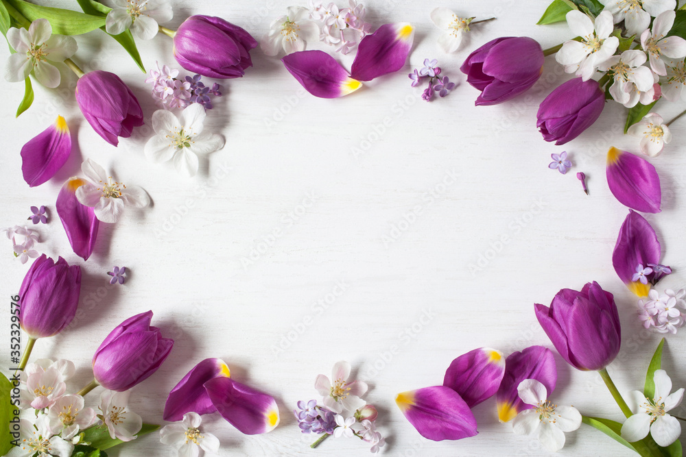 Purple tulips, lilac flowers, apple tree flowers on a wooden background. Space for congratulations text.