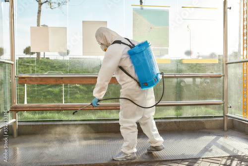 Save a life. Sanitization, cleaning and disinfection of the city due to the emergence of the Covid19 virus. Man in protective suit and mask at work near the bus stop photo