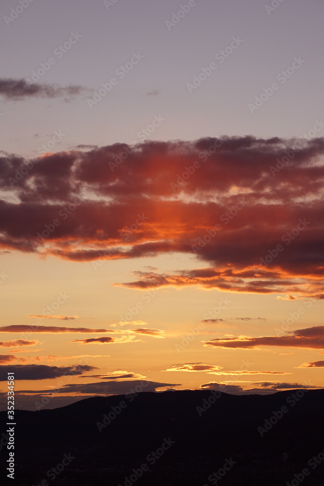 Obraz premium Luminous shades of yellow and orange streak the skies over the Mountains during sunset.