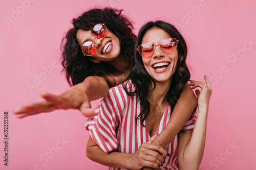 Unrestrained merriment of two girls captured on snapshot. Photos in pink shades of brunettes with beautiful curls, embracing in friendly way photo