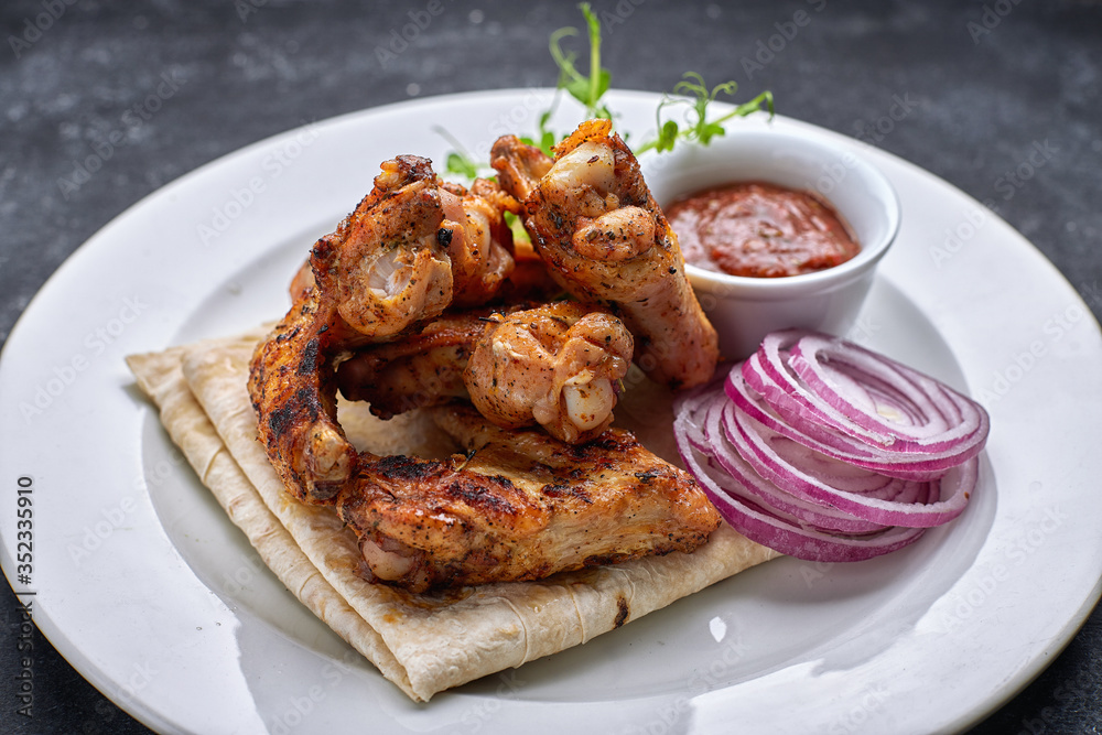 Grilled chicken wings with barbecue sauce, pita bread, microgreen and onion rings, on a white plate, against a dark background Grilled chicken wings with barbecue sauce, pita bread, microgreen and onion rings, on a white plate, against a dark background