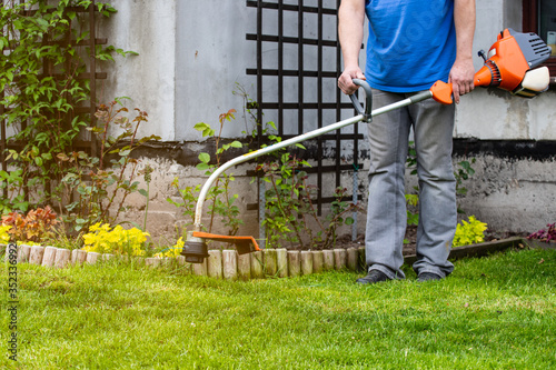 Man trimming grass with a small grass trimmer. The concept of a beautiful garden.