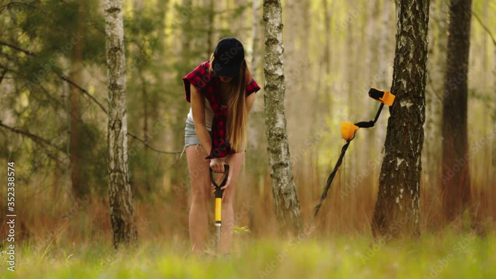 Young woman digging the treasure discovered with metal detector in the forest.