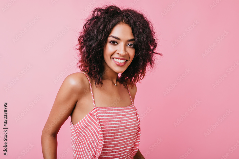 Slim dark-eyed African female model smiles sweetly, looking into camera. Portrait of girl in stylish outfit and beautiful jewelry on neck Slim dark-eyed African female model smiles sweetly, looking into camera. Portrait of girl in stylish outfit and beautiful jewelry on neck