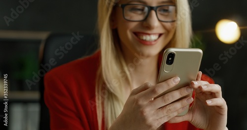 Close up of smartphone in hands of blonde businesswoman. Happy female texting message and typing on cellphone in cabinet.