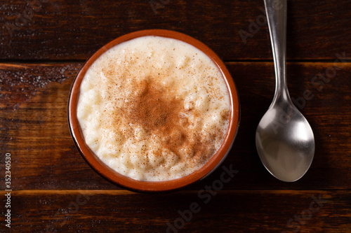 White corn cooked with milk known as canjica, canjicão or mungunza, in a rustic bowl on wooden table. Typical dish of Brazilian Party called Festa Junina.