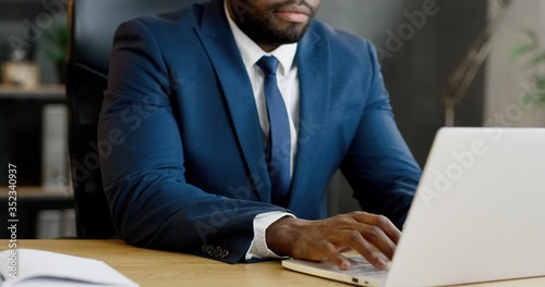 Fototapeta African American businessman sitting at table and working on laptop computer and typing on keyboard